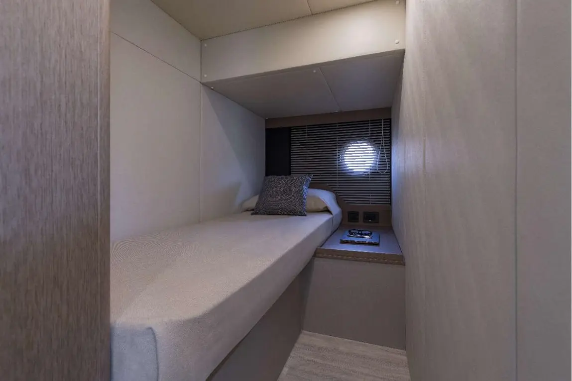 Modern cabin interior featuring a single bed, pillow, round window, bedside table, and power outlets.